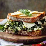 A sandwich with cheese and greens on a wooden cutting board.